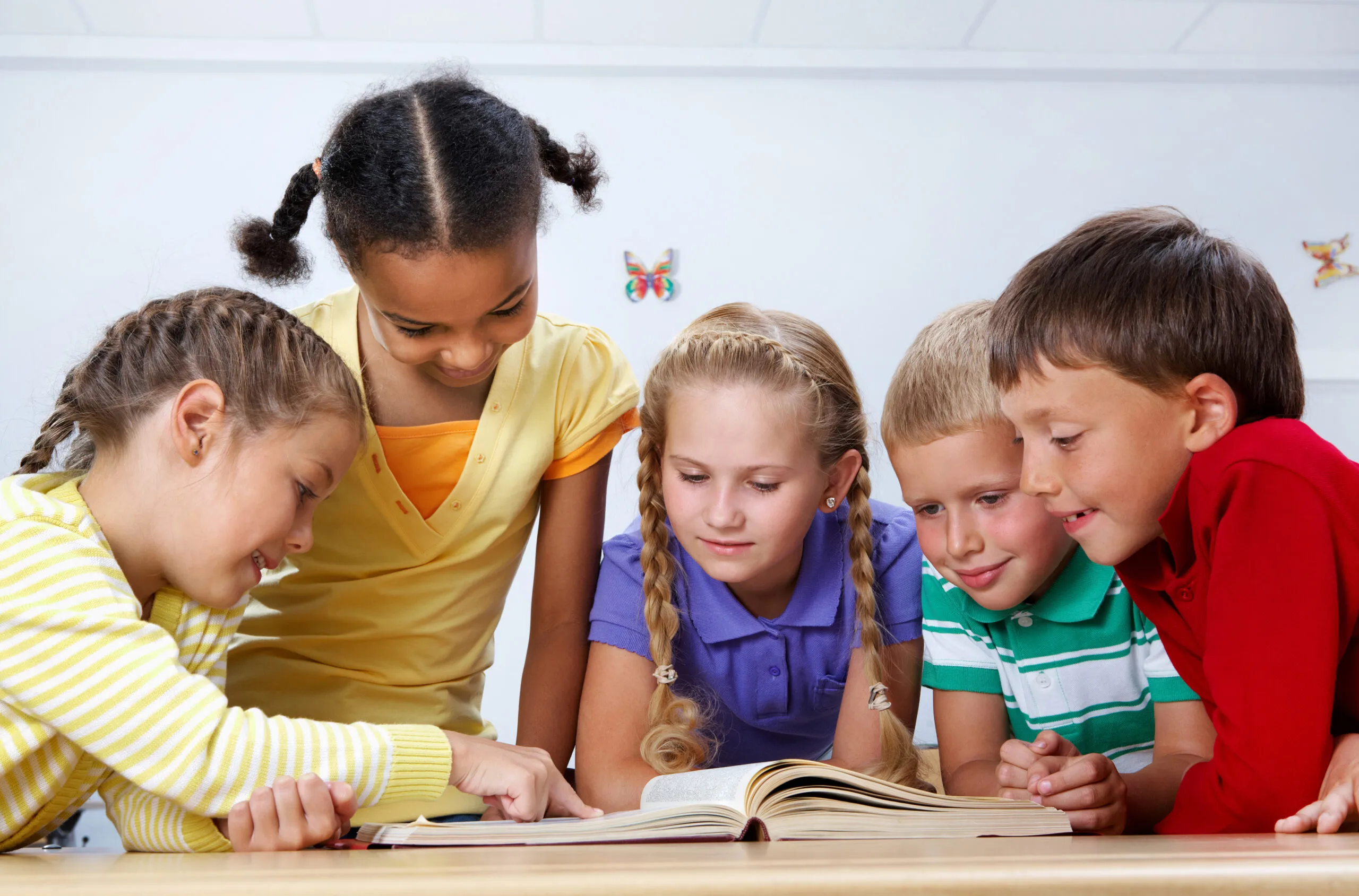 Five children gathered together around an open book, learning collaboratively
